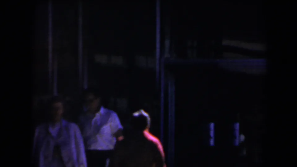 1958 Las Vegas home-movie frame showing shadowed people near a dark exterior entrance with colored night lighting.