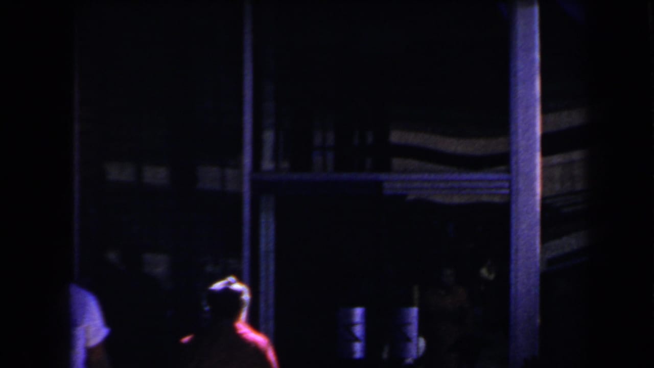 1958 Las Vegas frame with a red-coated figure near a dark building frontage under blue-purple light.