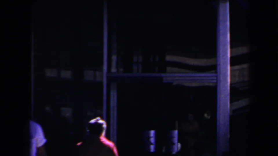 1958 Las Vegas frame with a red-coated figure near a dark building frontage under blue-purple light.