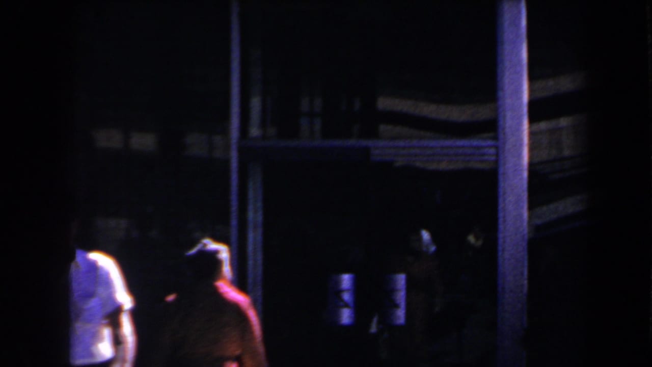 Low-light 1958 Las Vegas home-movie frame of two people moving past a shadowed exterior entrance.