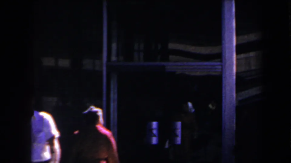 Low-light 1958 Las Vegas home-movie frame of two people moving past a shadowed exterior entrance.