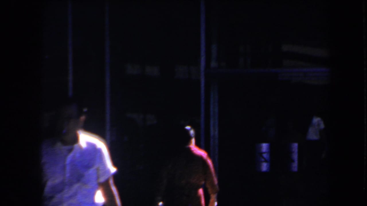 1958 Las Vegas night frame showing people beside a dark entrance with soft focus and colored light.