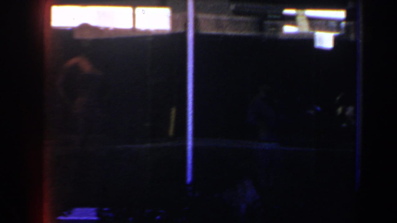 1958 Las Vegas 8mm frame showing a shadowed person near the left edge, bright overhead-like lights, and a blue vertical light strip.
