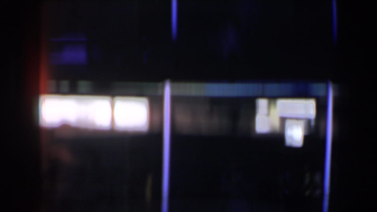 1958 Las Vegas 8mm frame with bright window-like panels, a blue vertical light line, and indistinct shapes in heavy shadow.