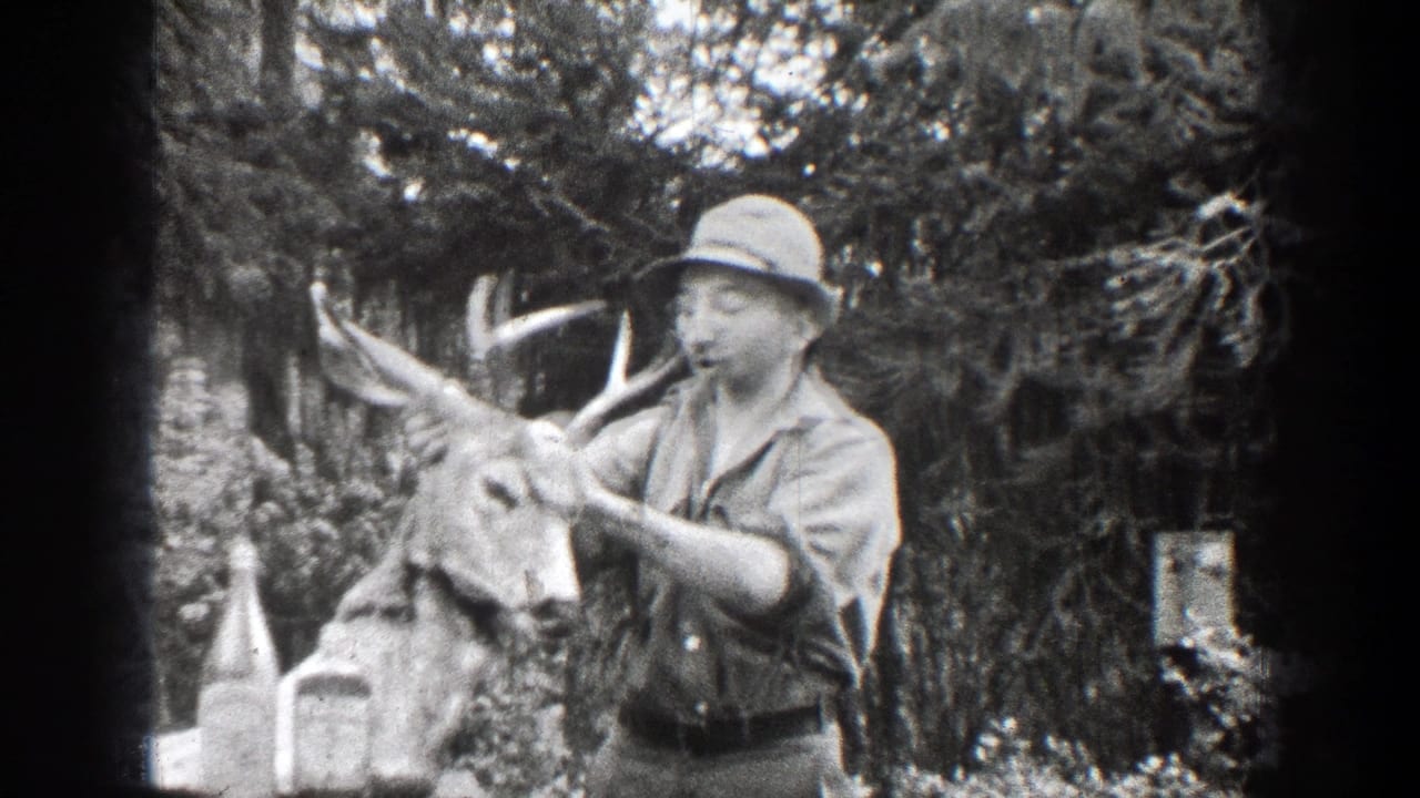 In 1939 Chelan, Washington home-movie footage, a man in a brimmed hat and button-front shirt holds a buck head with antlers beside bottles on an outdoor table.