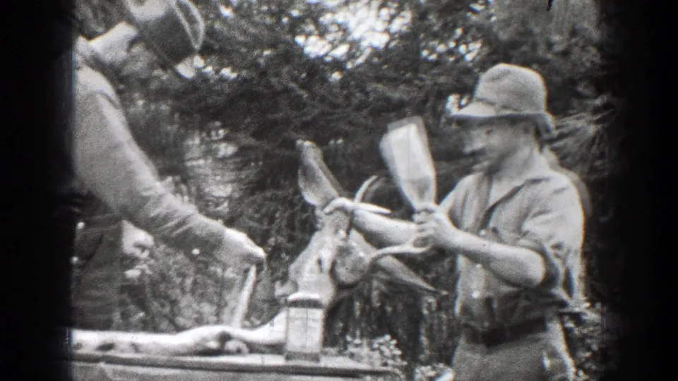1939 Chelan, Washington home-movie frame showing an adult man handling cloth beside a hunted deer in the woods.