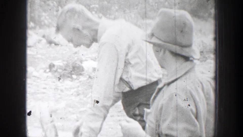 In 1939 Chelan, Washington footage, two men in brimmed hats lean close together in a rocky outdoor area.