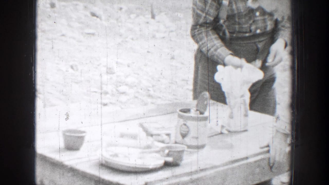 A man at an outdoor table handles a light-colored object near cups and plates.