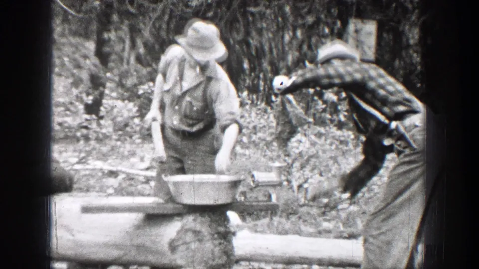 1939 Chelan, Washington 8mm frame showing one man at a basin as another reaches toward the outdoor cooking setup.