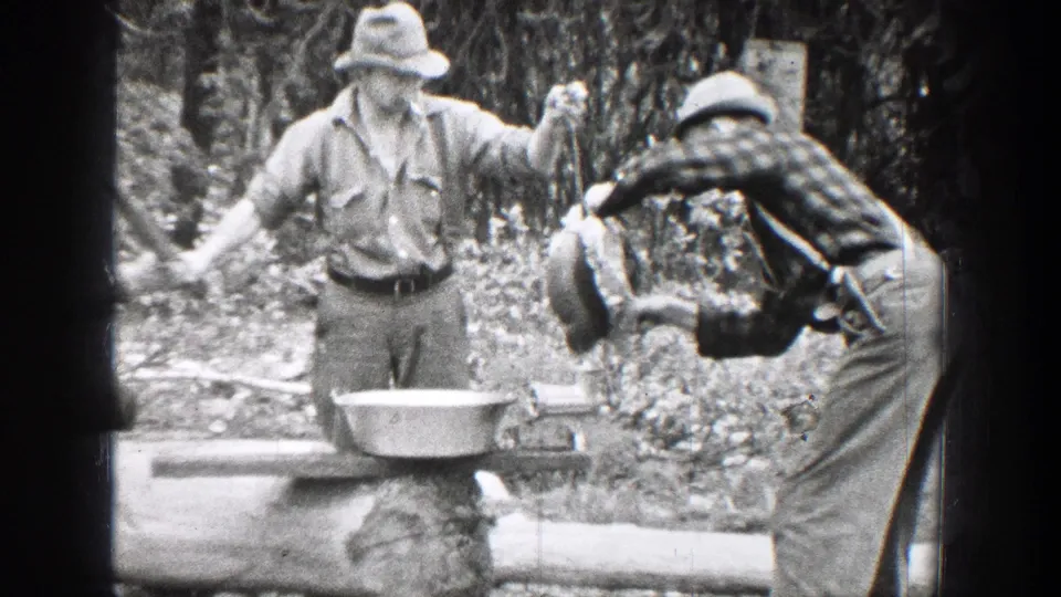 1939 Chelan, Washington frame of two men at a makeshift wooded cooking station with a basin, tools, and work clothes visible.