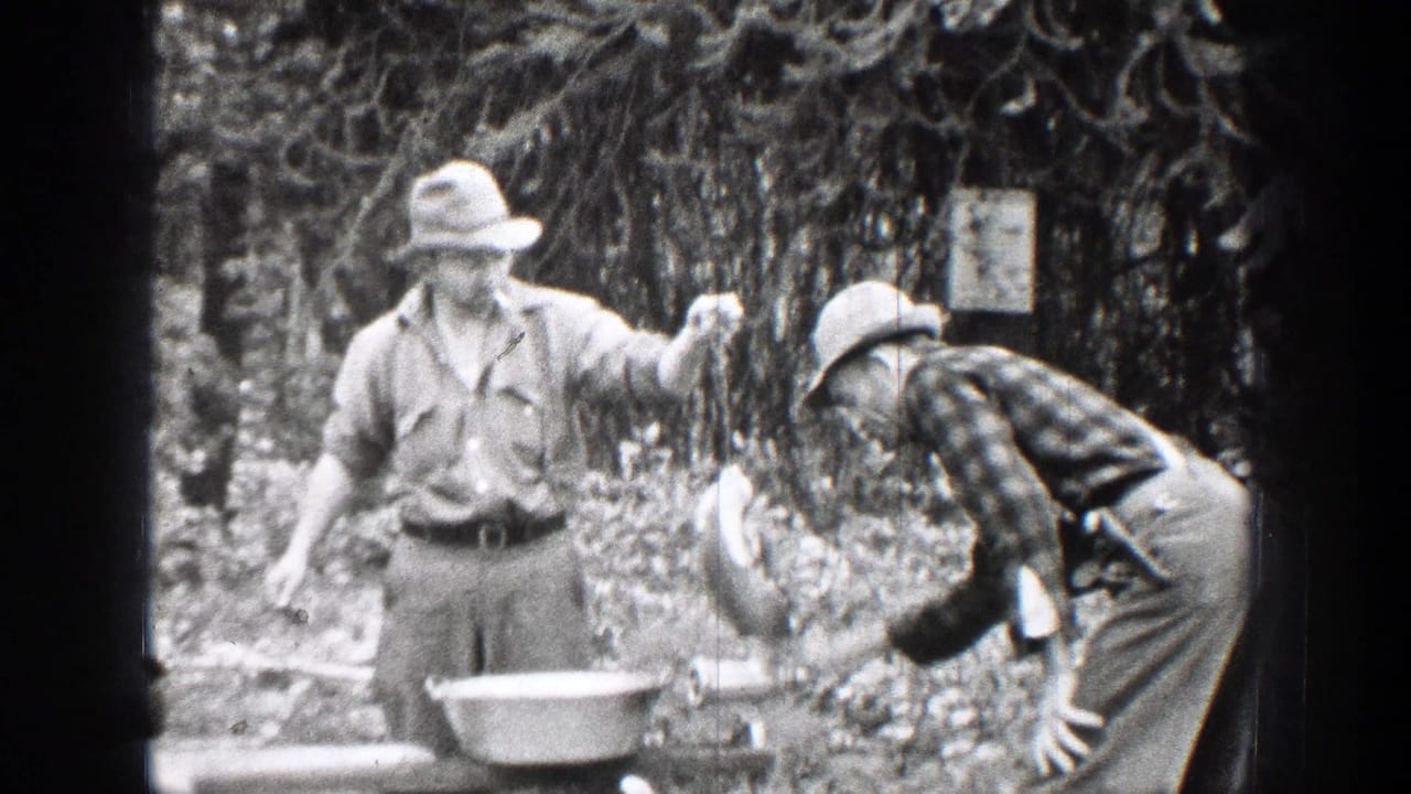 Man holds game meat while another leans toward a grinder in the woods.