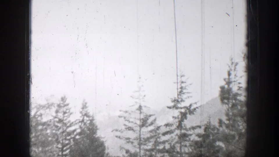 1939 Chelan, Washington home-movie frame with evergreen treetops, haze, and hills beyond a dark window edge.