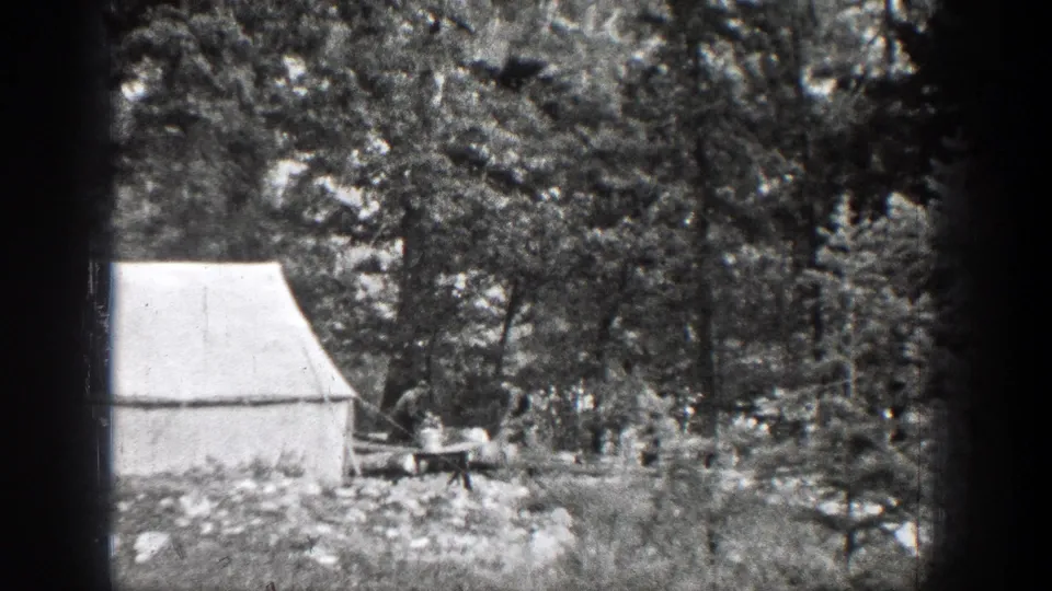 The campsite remains framed through dark 8mm borders, showing a canvas tent, forest trees, rocky ground, and a small wood-handling area near Chelan, Washington.