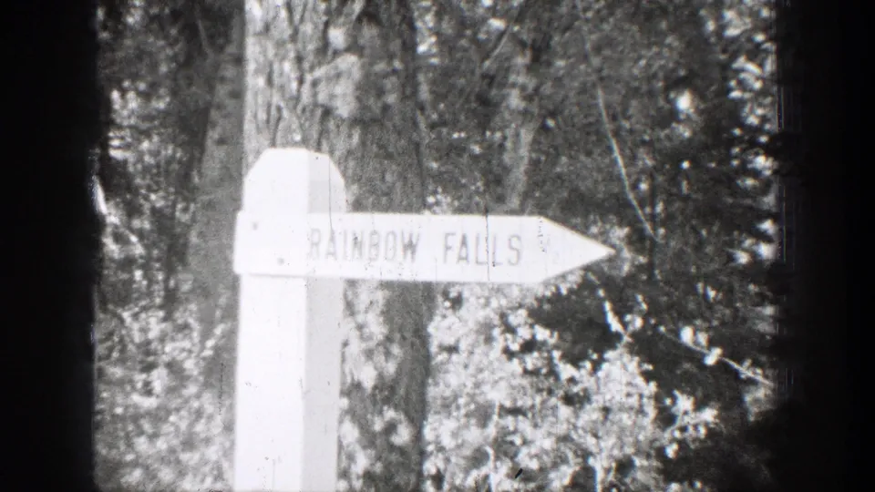 1939 Chelan-area home-movie frame showing a white Rainbow Falls direction sign set against dense trees.