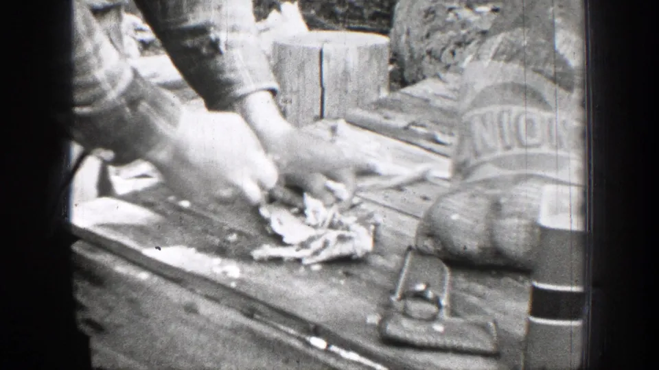 In 1939 Chelan, Washington home-movie footage, a person cuts meat outdoors on a wooden board beside bags and utensils.