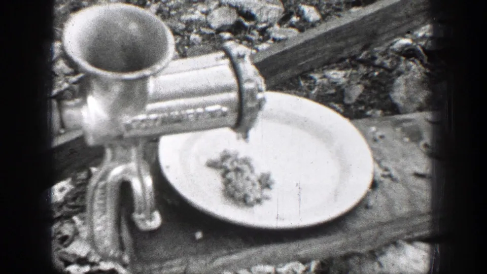 A hand-cranked metal meat grinder processes meat onto a white plate in the 1939 Chelan home-movie scene.