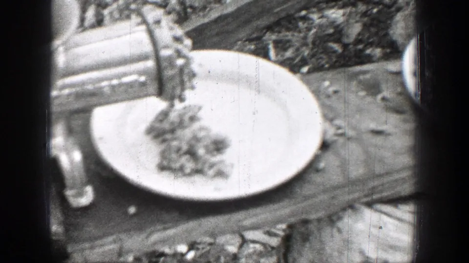 The metal grinder continues feeding ground meat onto a white plate, with the outdoor work surface visible around it.