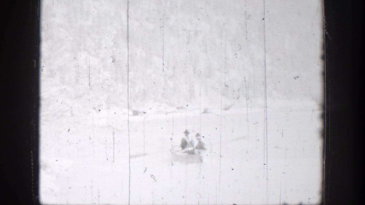 Two distant people sit in a small rowboat on a bright Chelan, Washington lake in 1939 home-movie footage.