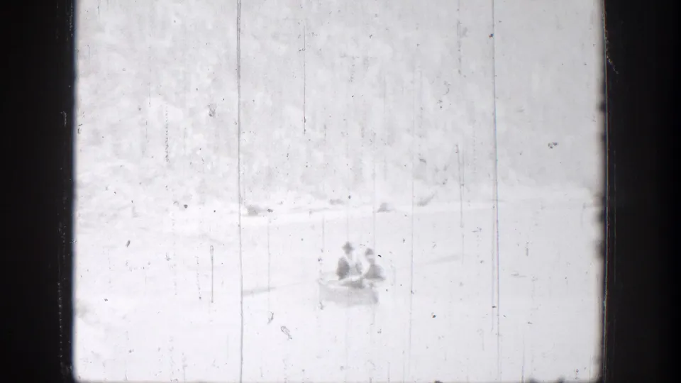 Two distant people sit in a small rowboat on a bright Chelan, Washington lake in 1939 home-movie footage.