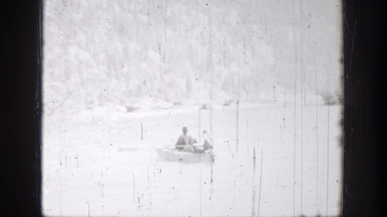 Small rowboat with two people near a pale shoreline.
