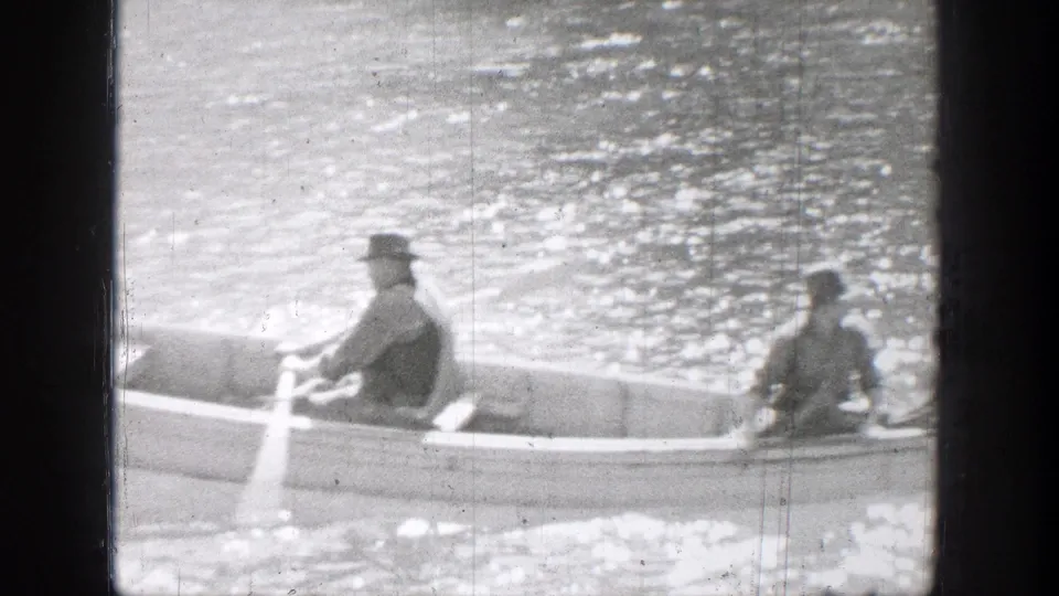 Two hat-wearing people ride in a small rowboat on sunlit water in 1939 Chelan, Washington home-movie footage.