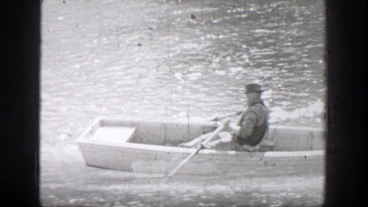 A person rows a small boat across rippling water.