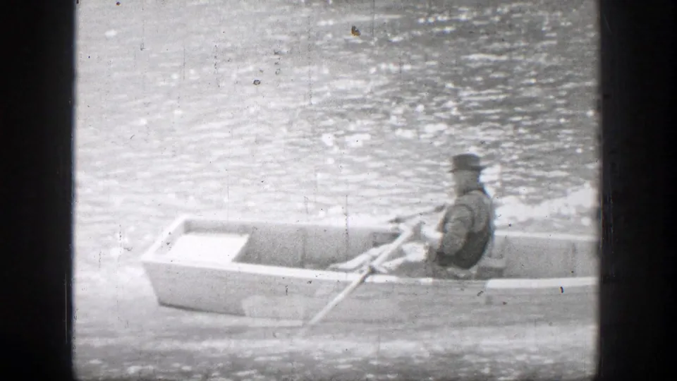 A hat-wearing rower moves a small boat across shimmering water in Chelan, Washington, with the passenger mostly out of view.