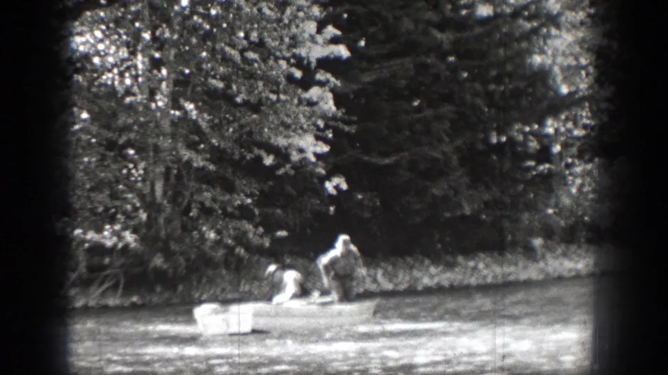 The rowboat appears farther from the camera near a wooded shoreline in the Chelan, Washington home-movie scene.