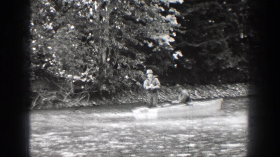 1939 Chelan, Washington footage shows two men fishing from a small boat beside a tree-lined pond bank.