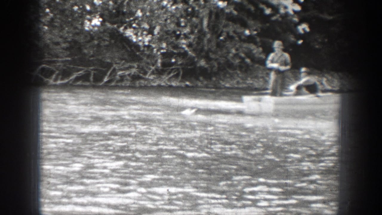 1939 Chelan, Washington home-movie frame showing two adult men fishing from a rowboat on rippled river water.