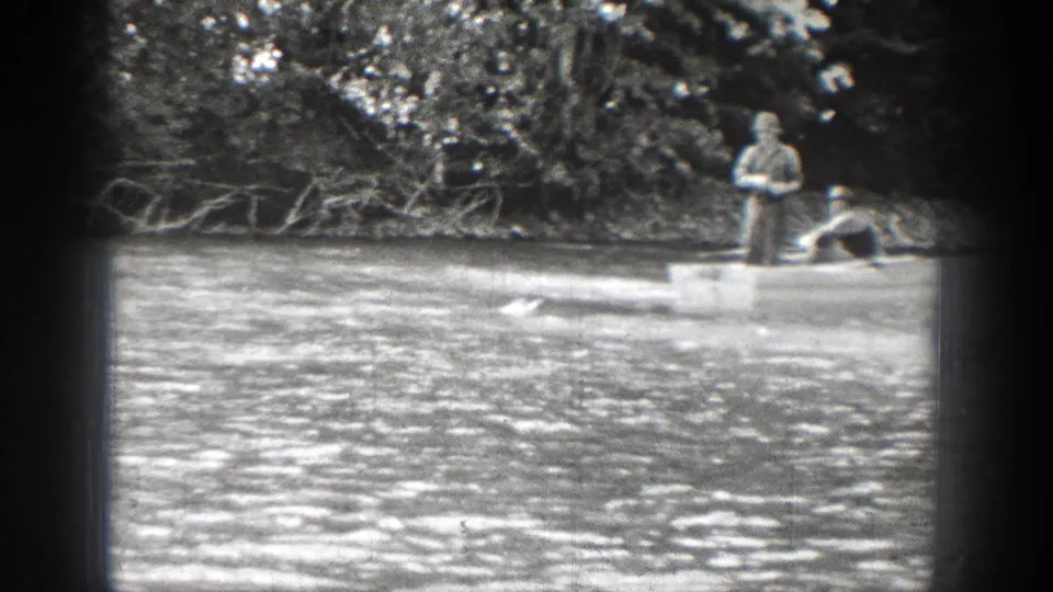1939 Chelan, Washington home-movie frame showing two adult men fishing from a rowboat on rippled river water.