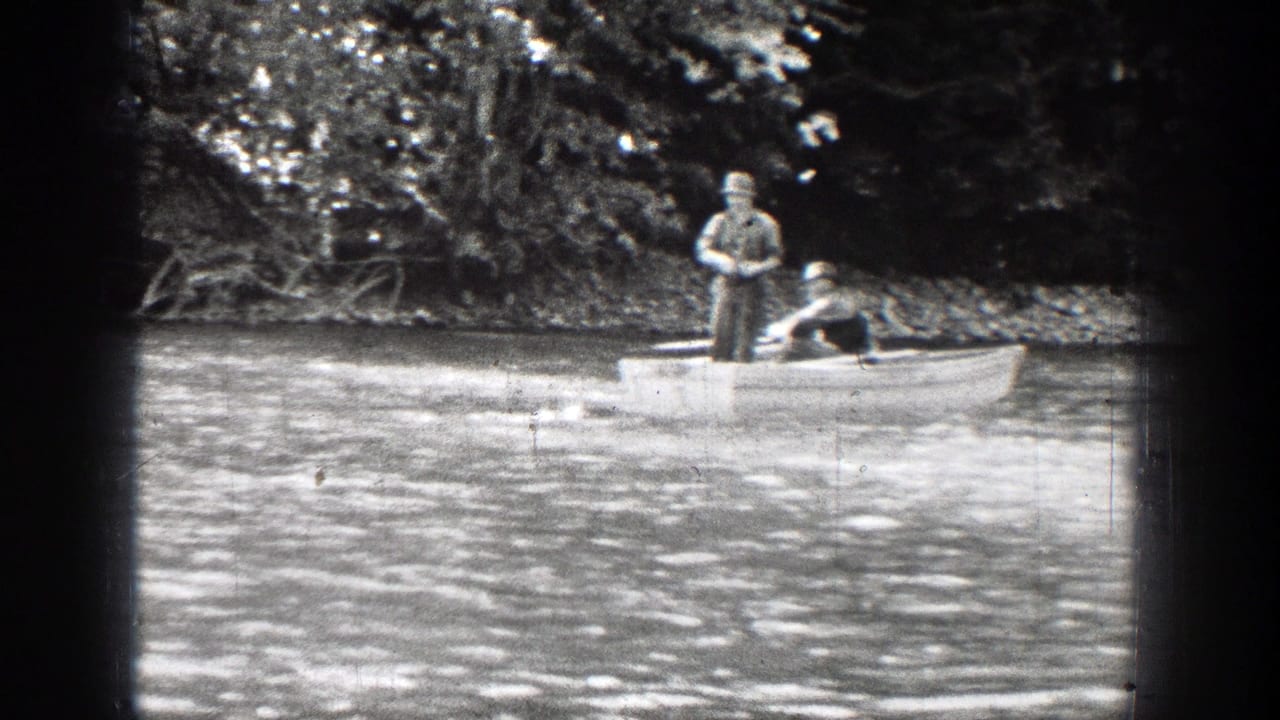 Two men appear in a small rowboat on a Chelan river, with one standing and fishing near a wooded shoreline.