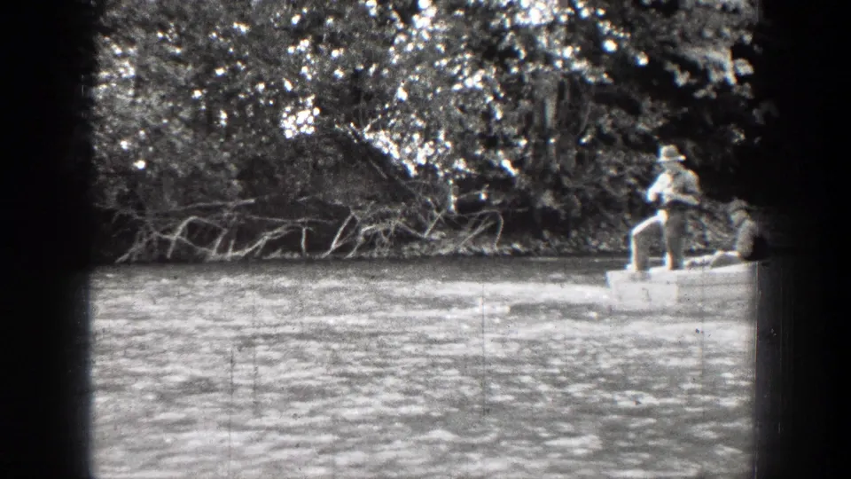 The rowboat moves toward the frame edge while the wooded Chelan riverbank and rippled water fill most of the view.