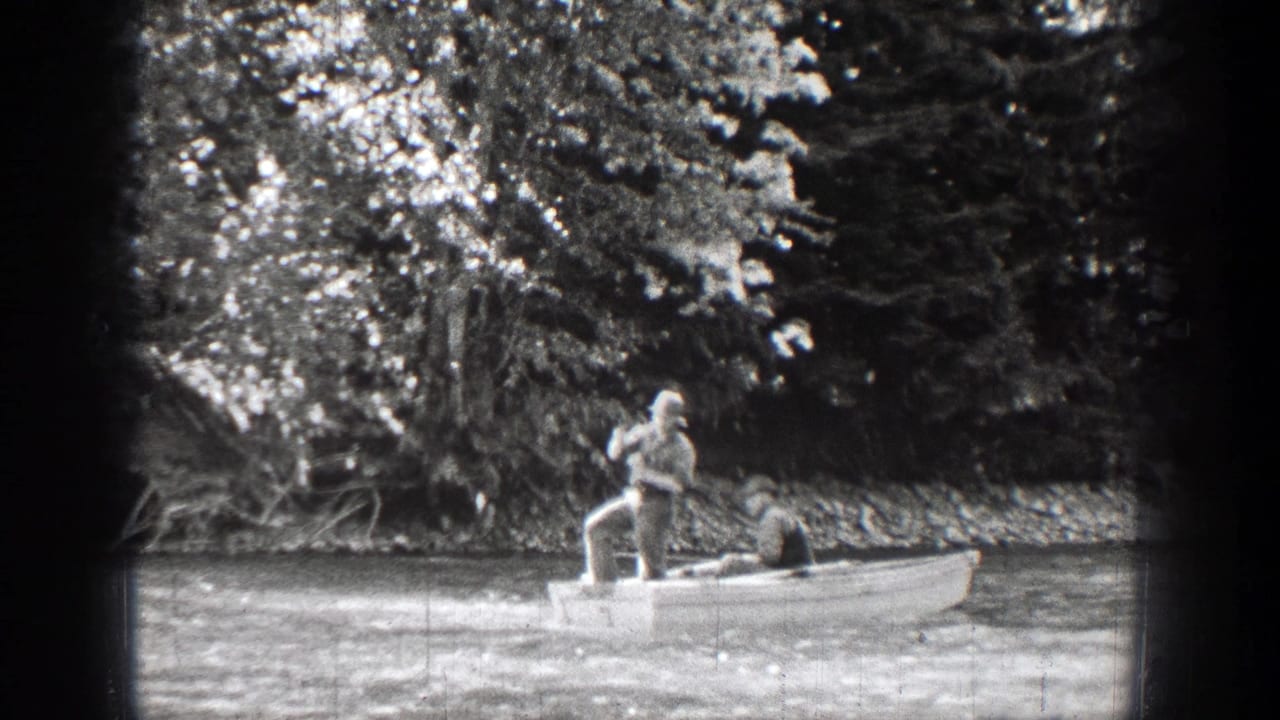 In 1939 Chelan, Washington footage, one man stands at the stern with an oar while another sits in the bow near a wooded riverbank.