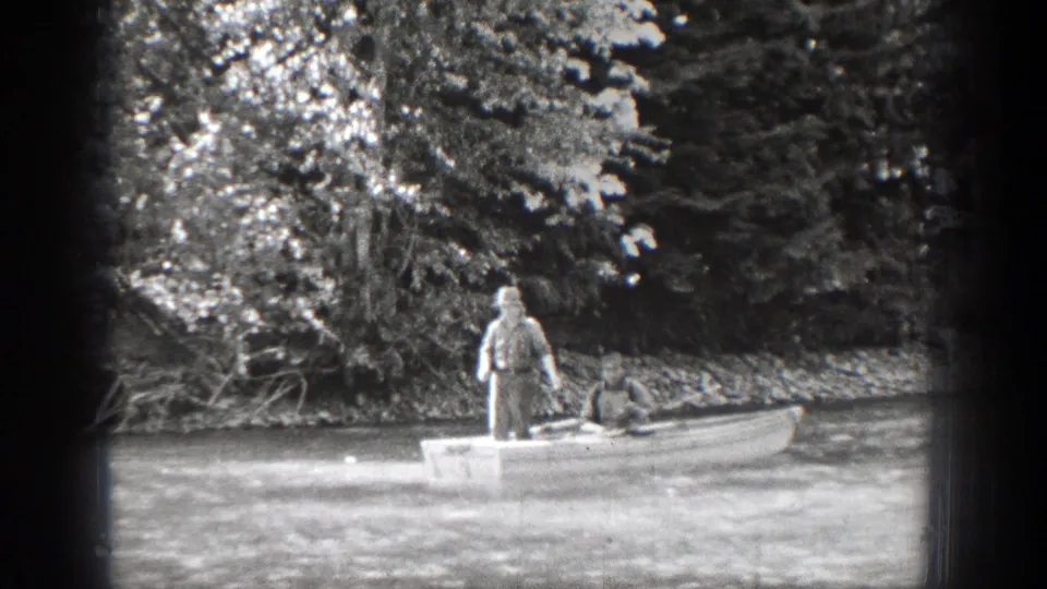 The Chelan home-movie frame shows two men in a low rowboat, with the stern man upright and the bow passenger leaning down.