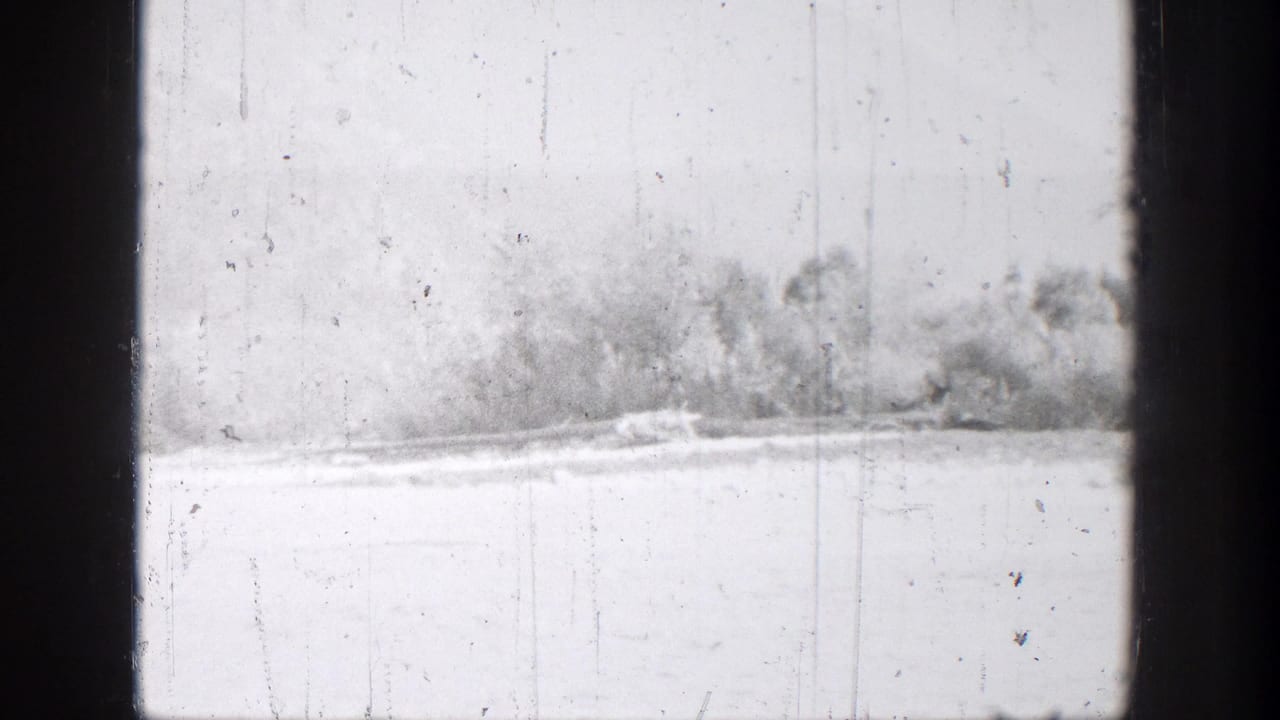Bright 8mm view of the Chelan lakeshore with distant trees, pale water, and dark edges in the filmed frame.