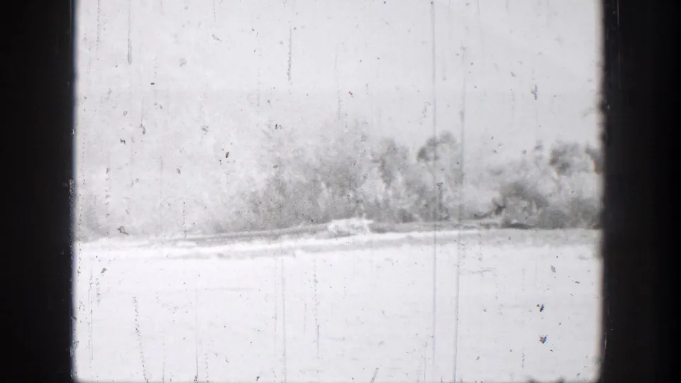 Bright 8mm view of the Chelan lakeshore with distant trees, pale water, and dark edges in the filmed frame.