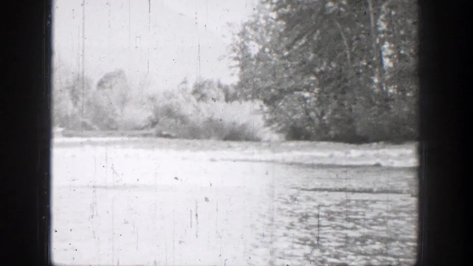 Black-and-white 8mm frame of a calm river bordered by brush and trees in Chelan, Washington.