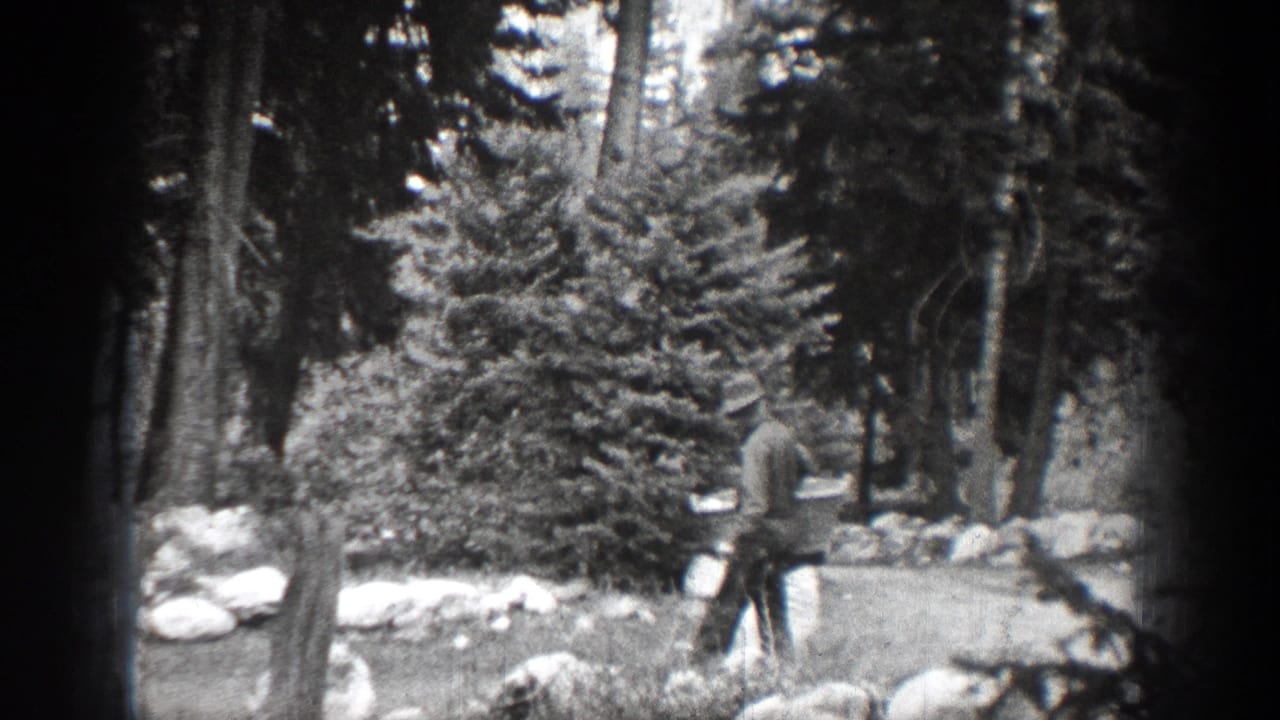 Man in a hat walks through a wooded area carrying a light-colored bag.
