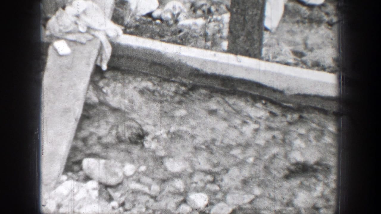 Rocky outdoor ground in the Chelan 1939 8mm clip, with a concrete border, vertical post, and light cloth or fabric near the edge.