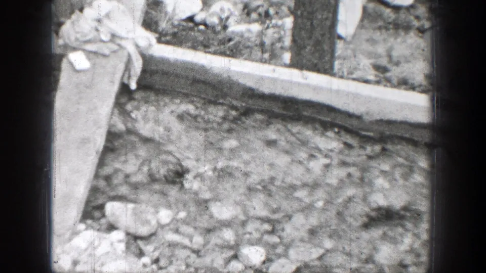 Rocky outdoor ground in the Chelan 1939 8mm clip, with a concrete border, vertical post, and light cloth or fabric near the edge.