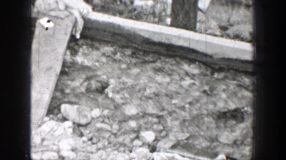 A rocky stream bed or damp ground area appears beside a concrete border in black-and-white 1939 Chelan home-movie footage.