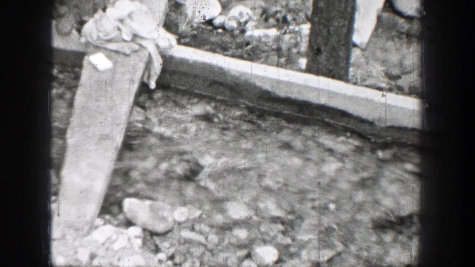 1939 Chelan, Washington 8mm frame showing a rough wooden plank crossing a clear rocky stream near boards and cloth.