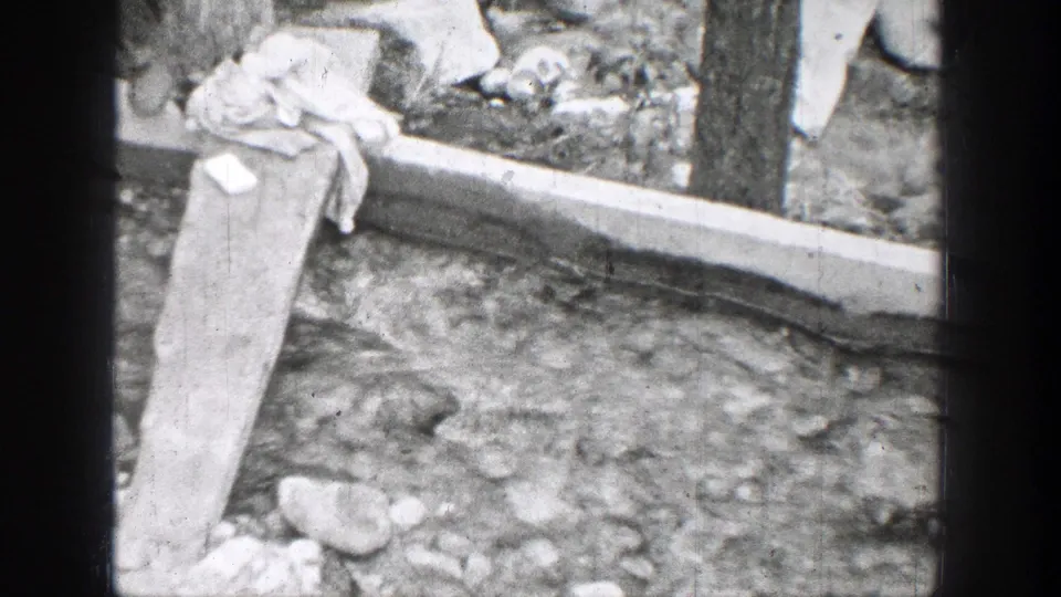 1939 Chelan, Washington view of a plank over running water, with rocks, boards, and fabric at the creek edge.