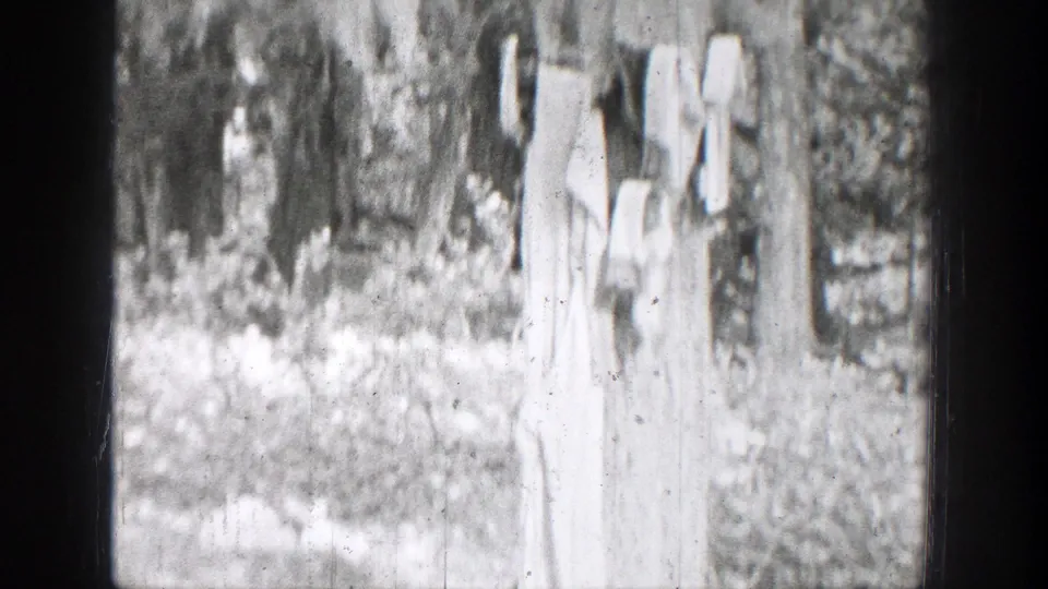 1939 Chelan, Washington frame with light-colored laundry hanging between trees near a wooded creekside area.