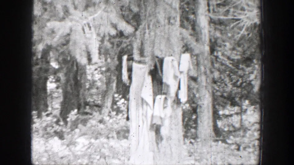 1939 Chelan, Washington home-movie frame showing laundry on a line among trees beside brush and creekside stones.