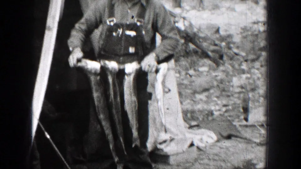 Two adult fishermen in Chelan, Washington, stand in work clothes and hats while displaying their catch on 1939 8mm film.