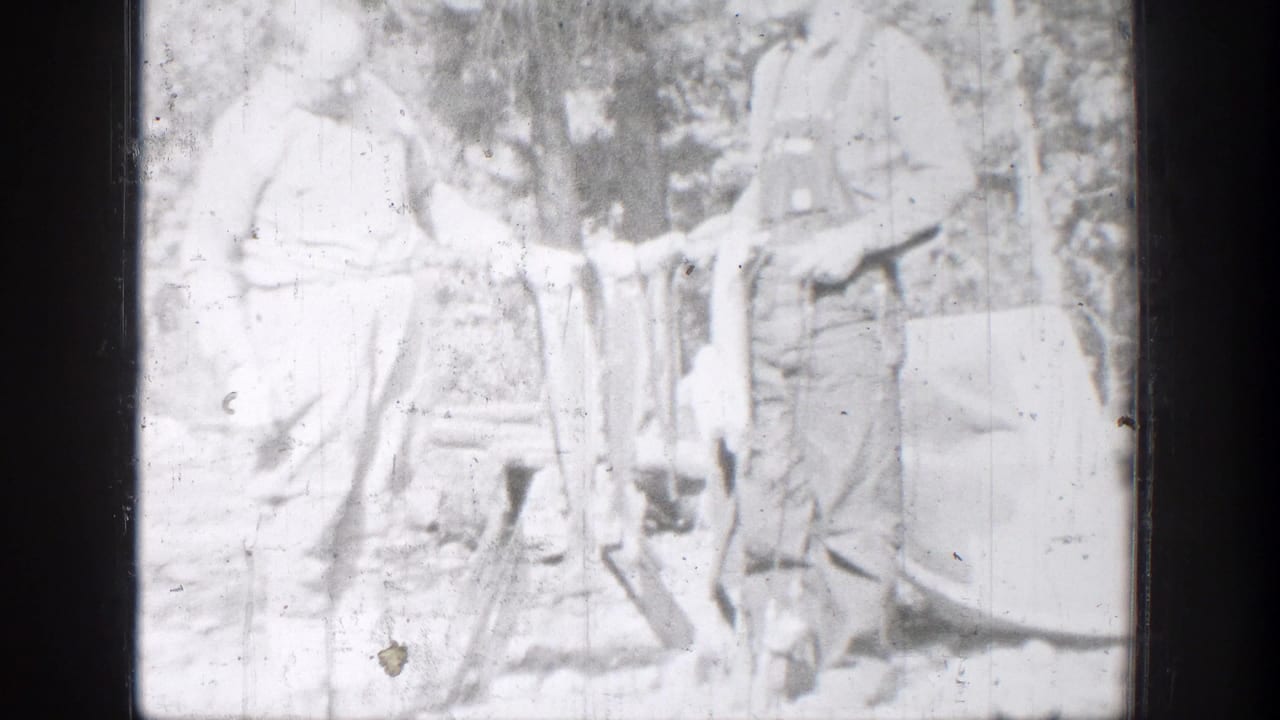 A bright 1939 home-movie frame shows two Chelan fishermen standing together with fish in front of trees and brush.