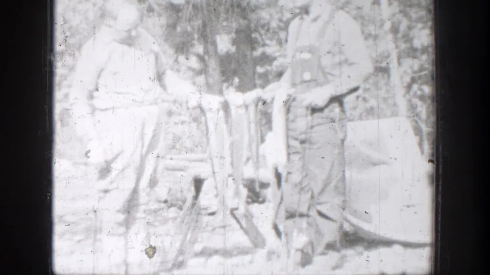 A bright 1939 home-movie frame shows two Chelan fishermen standing together with fish in front of trees and brush.