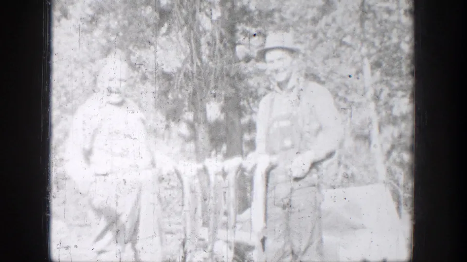 One fisherman smiles toward the camera while standing with another person and several fish in a wooded Chelan setting.